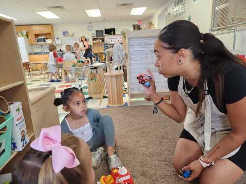 Child care worker Marci Then helps her daughter, Mila, 4, put away toys to get ready for circle time at the Little Learners Academy in Smithfield, R.I. A new study highlights the high cost of child care.