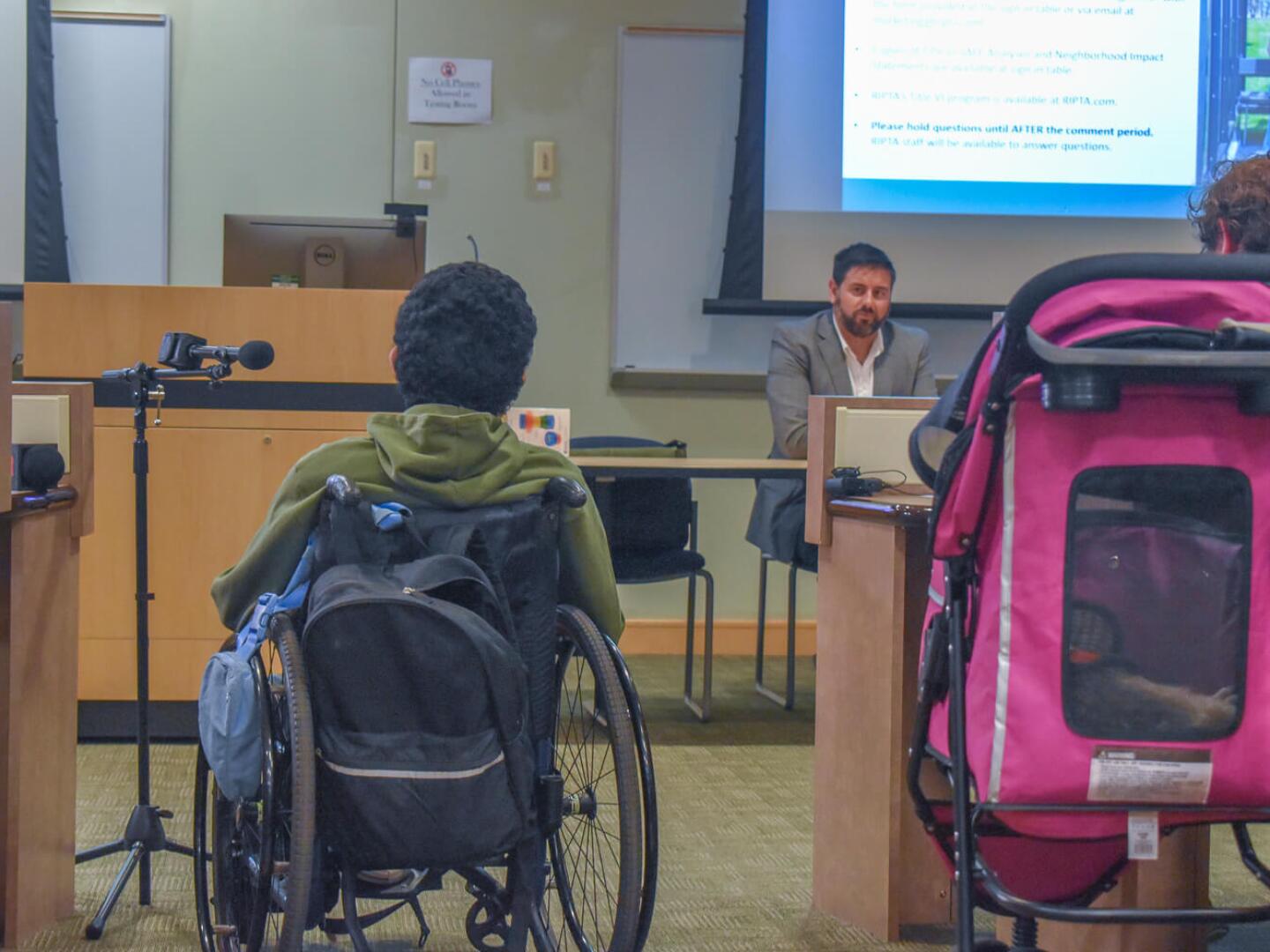 Devin Guirales of Central Falls, foreground, speaks against proposed service bus cuts in front of Rhode Island Public Transit Authority CEO Christopher Durand at a public hearing hosted at the Community College of Rhode Island’s Warwick campus on July 28, 2025.