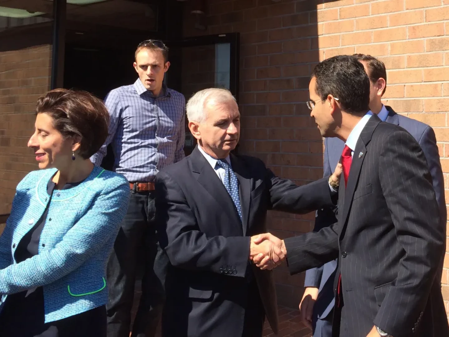 Hyers, in back, looks on as Gina Raimondo, Jack Reed and Angel Taveras exchange pleasantries during a 2014 Democratic unity event.