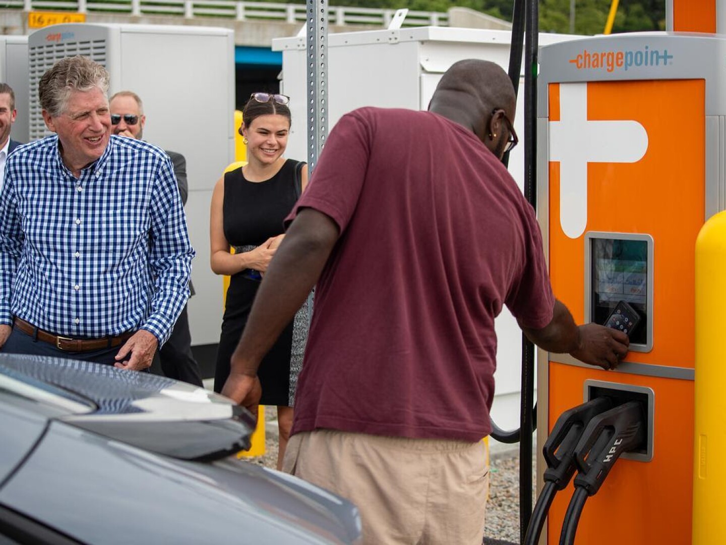 Gov. Dan McKee, left, looks on as a new Direct Current Fast Charger for electric vehicles is used at the Route 117 Park & Ride in Warwick along Interstate 95 during a July 17, 2024, ceremony marking the completion of the first phase of the alternative fuel corridor under the National Electric Vehicle Infrastructure Program.